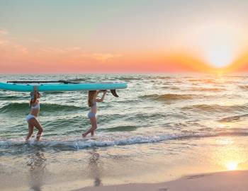 two girls carrying a paddle board on the beach