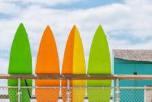 Stack row of multicolored colorful stand up surfing boards on railing fence.