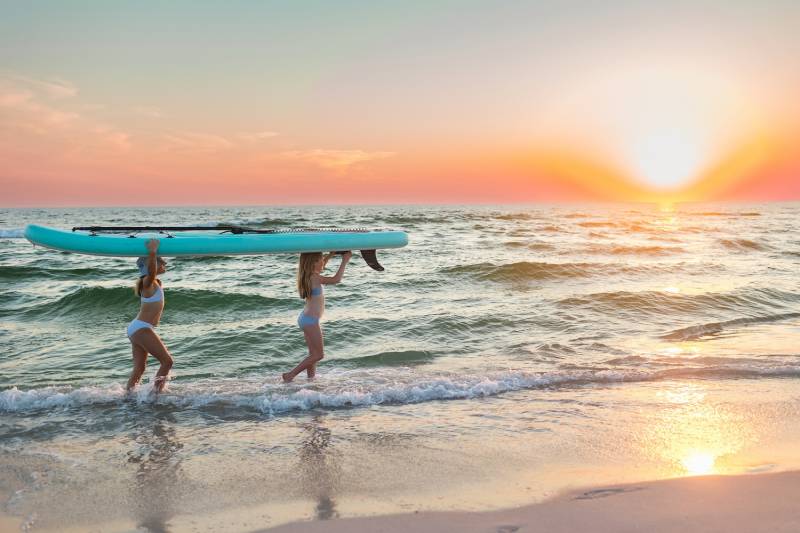 two girls carrying a paddle board on the beach