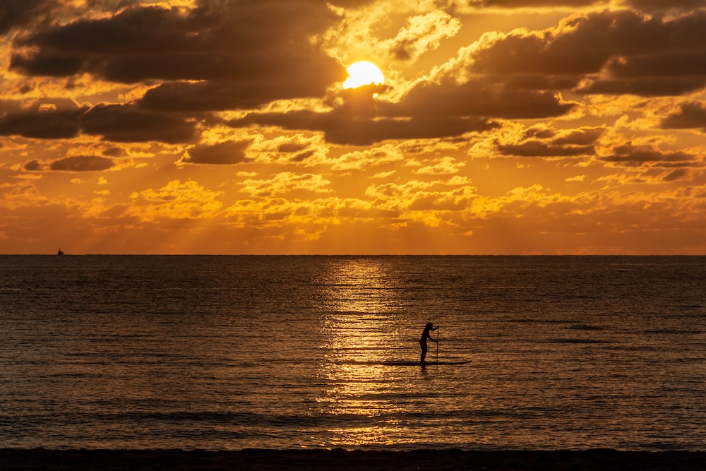 silhouette of a woman on a paddle board on the ocean at sunrise